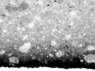 Figure 6. Section through another black crucible, where abundant translucent sand grains are present within the ceramic, but there is no graphite at all. The surface (bottom layer), however, appears blackened. Photomicrograph under polarised light, 50x magnification.